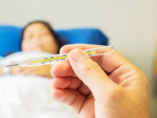 Doctor checking a thermometer to monitor a patient's body temperature during fever diagnosis and treatment.